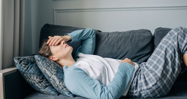 Frau, hält sich eine Hand auf das Gesicht und liegt auf der Couch.