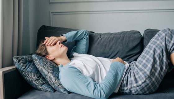 Frau, hält sich eine Hand auf das Gesicht und liegt auf der Couch.