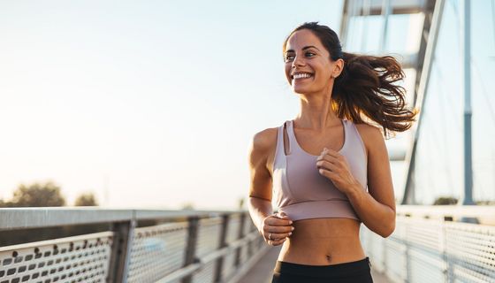 Eine Frau joggt strahlend eine Brücke entlang.