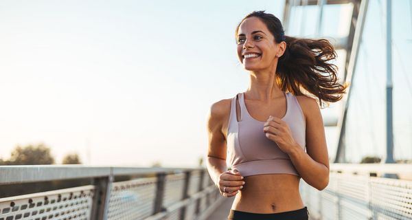 Eine Frau joggt strahlend eine Brücke entlang.