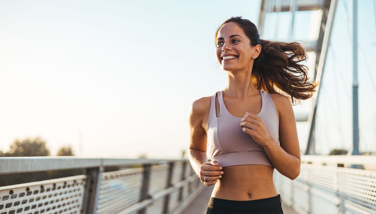 Eine Frau joggt strahlend eine Brücke entlang.