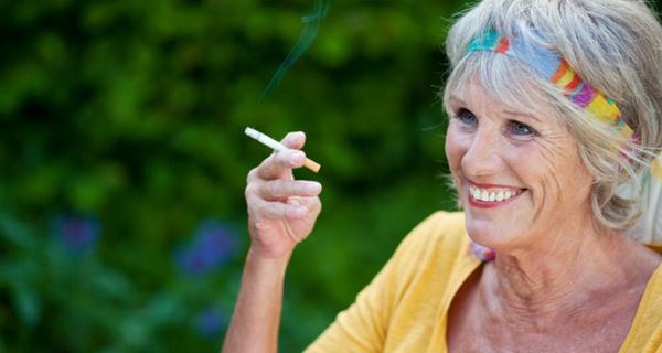 Rauchende Seniorin mit gelbem Top im Freien