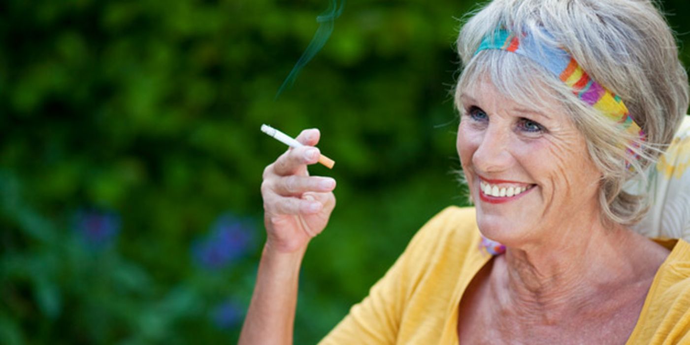 Rauchende Seniorin mit gelbem Top im Freien
