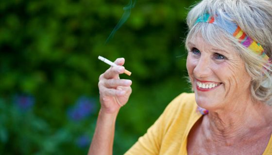 Rauchende Seniorin mit gelbem Top im Freien