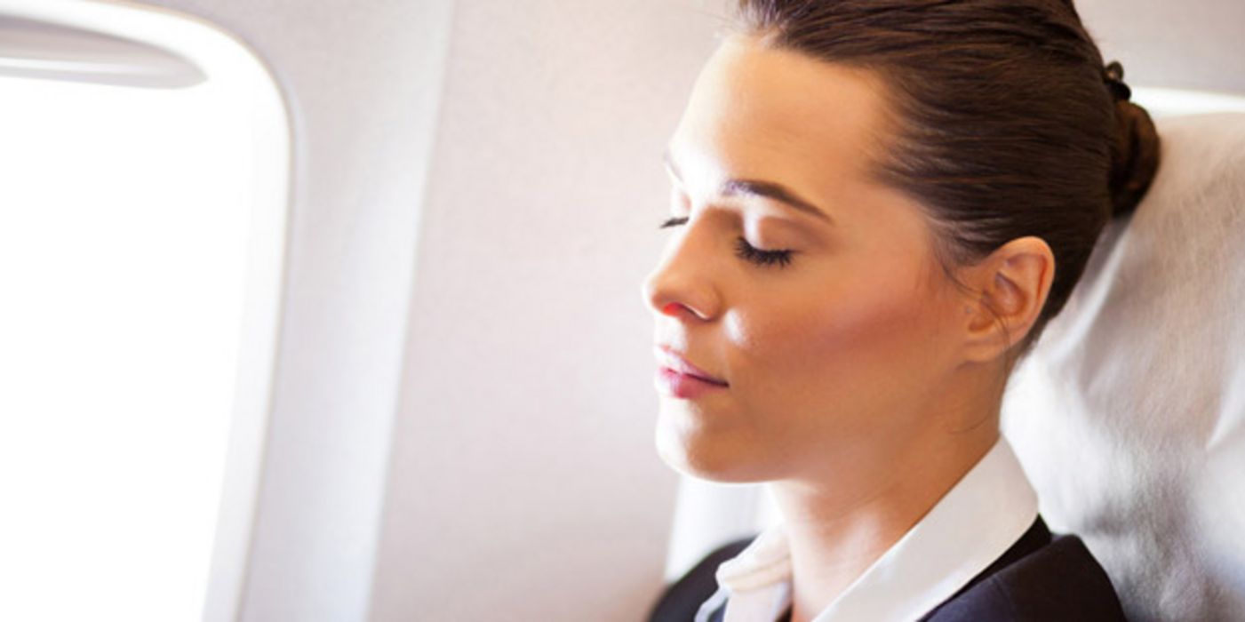 Junge Frau mit geschlossenen Augen sitzt im Flugzeug am Fenster
