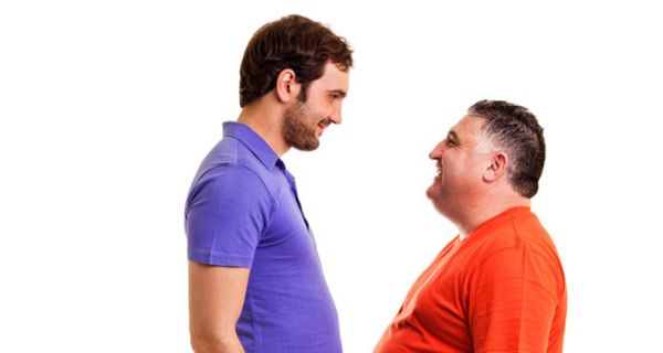 Großer, junger, schlanker Mann in blauem T-Shirt und kleiner, dicker, älterer Mann in rotem T-Shirt stehen sich gegenüber