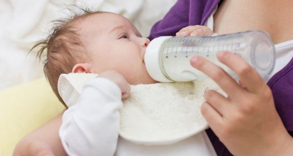 Bildausschnitt: Mutter (Brustbild) hält Säugling im Arm und gibt ihm die Flasche