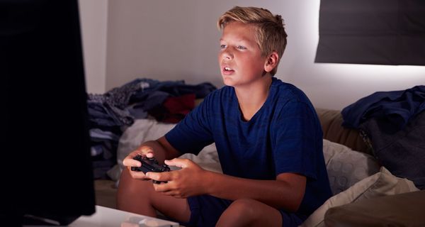 Junge mit Spielkonsole in der Hand starrt auf seinen Fernseher