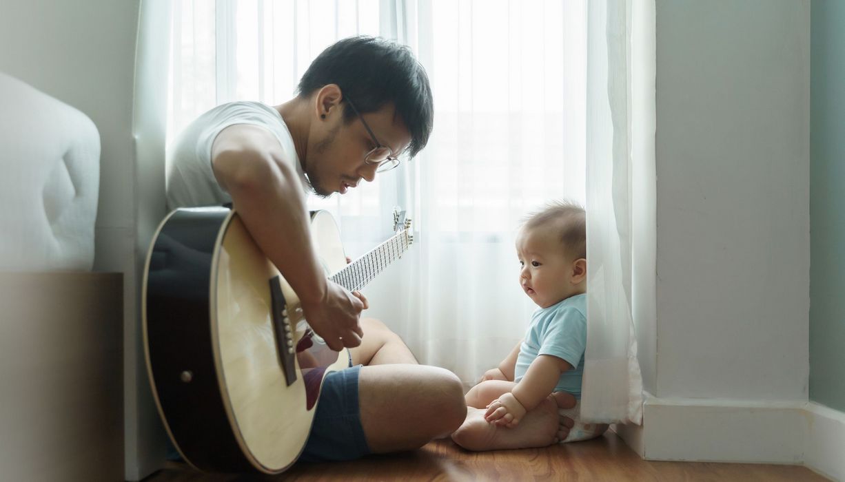 Vater, spielt für sein Kind Gitarre.