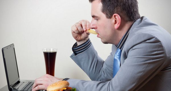 Mann sitzt vor einem Laptop und isst Fastfood