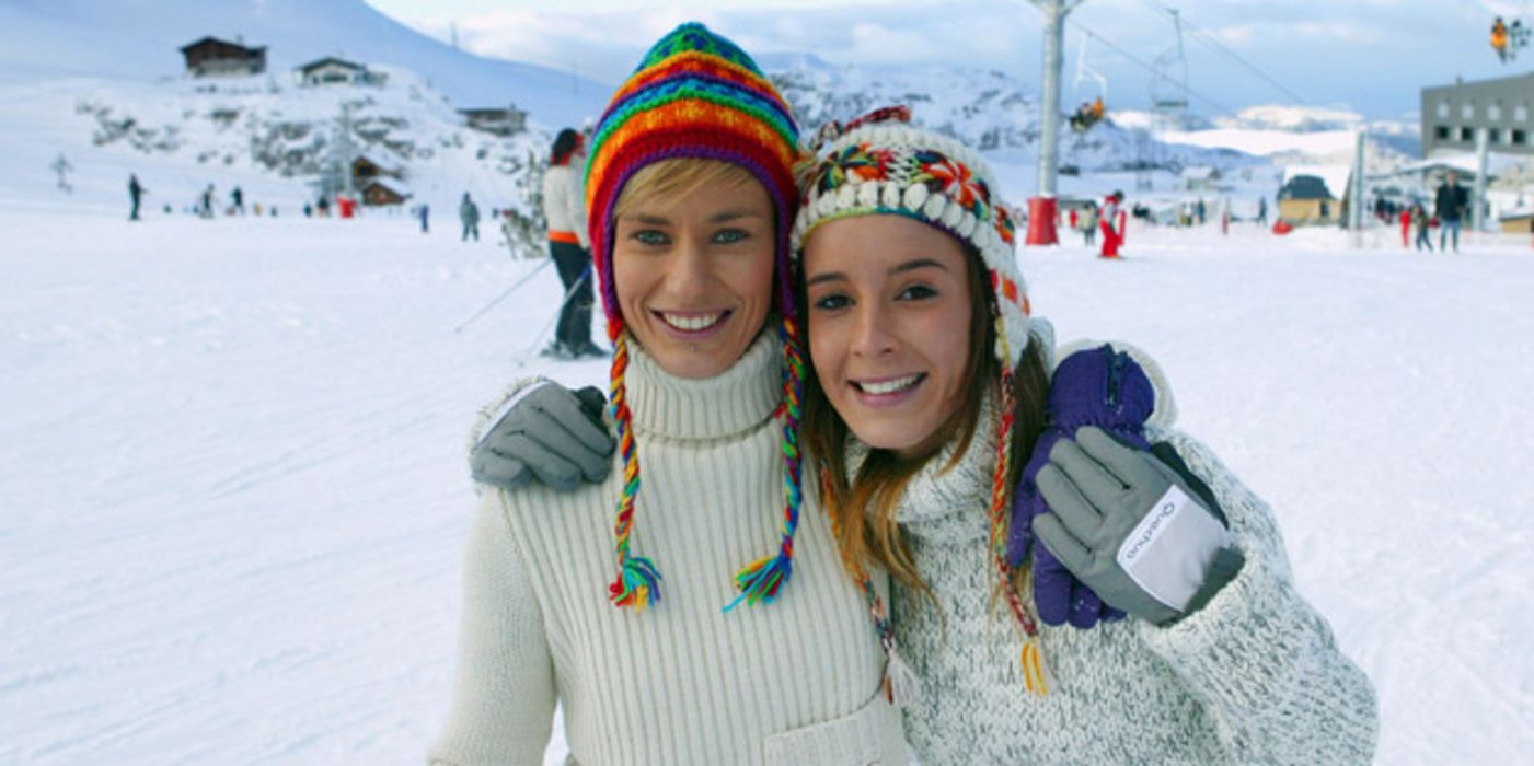 Zwei junge Wintersportlerinnen mit Mützen auf der Piste
