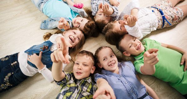 Sieben fröhliche Kinder liegen sternförmig auf dem Boden.