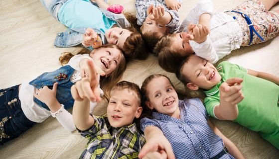 Sieben fröhliche Kinder liegen sternförmig auf dem Boden.