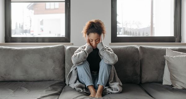 Junge Frau, sitzt auf einer Couch und stützt ihre Hände in den Kopf.