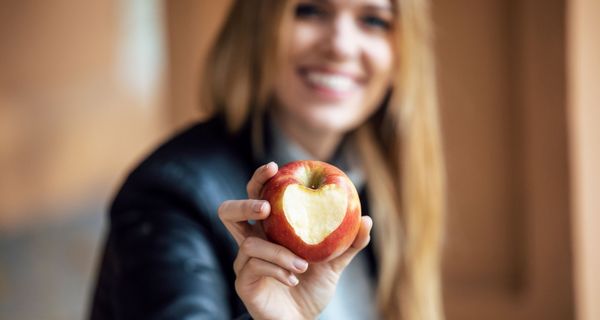 Junge Frau hält einen Apfel in die Kamera, der einen herzförmigen Biss hat.
