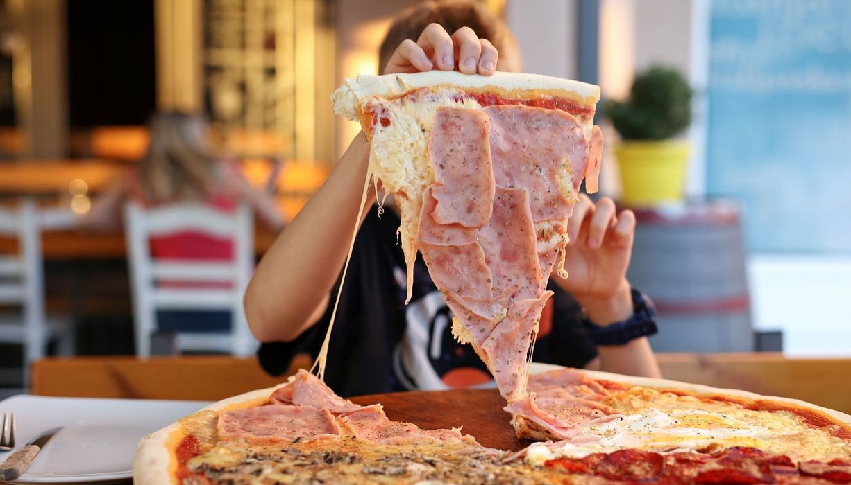 Junge, nimmt sich ein großes Stück Pizza.