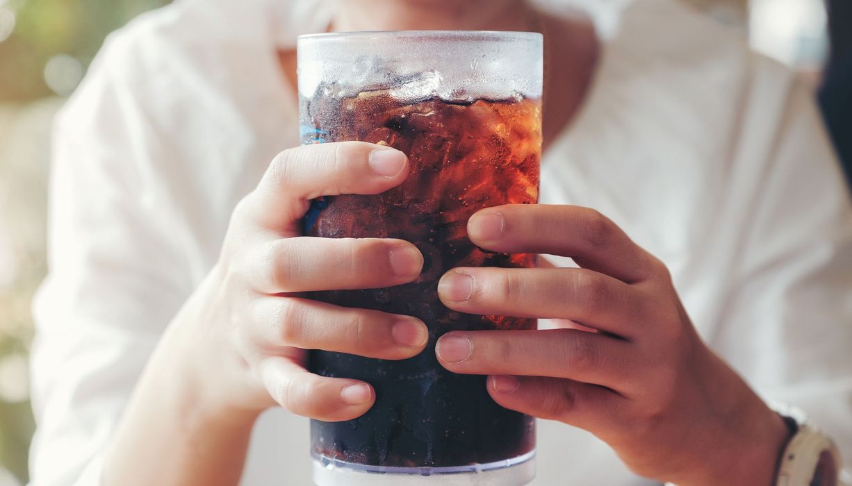 Frau, hält ein Glas Cola in der Hand.