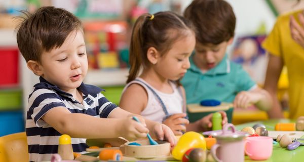 Kita-Kinder sitzen am Tisch einer Spielzeugküche.