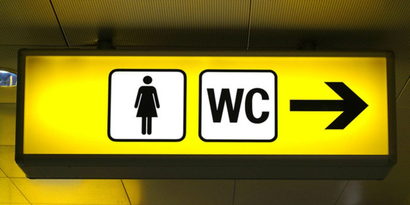 Gelbes Toilettenhinweisschild Schwarzes Symbol Frau, schwarzer Pfeil