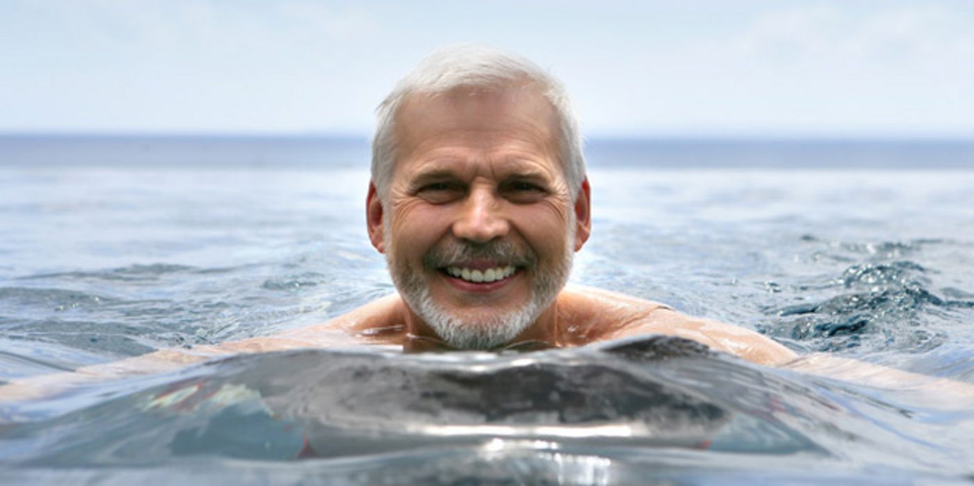Portraitfoto, älterer Mann schwimmt lachend im Meer
