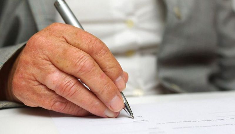 Hand eines älteren Mannes beim Schreiben mit einem silberfarbenen Tintenroller