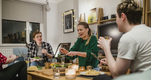 Gruppe von Freunden sitzt um einen Couchtisch herum und isst zusammen.