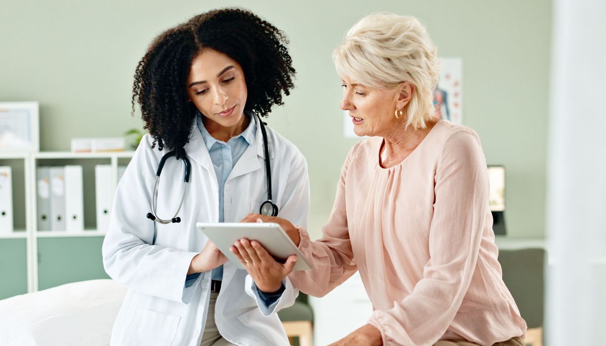 Ärztin zeigt Patientin etwas auf einem Tablet.