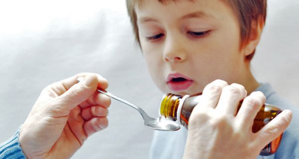 Junge, ca. 6 Jahre alt, bekommt mit einem Löffel aus einer Medizinflasche ein Medikament