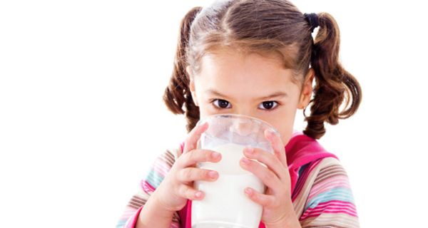 Kleines Mädchen trinkt Milch aus einem großen Glas