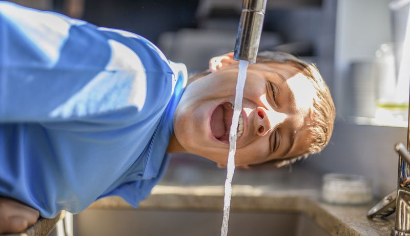 Junge, trinkt Wasser aus dem Hahn. 