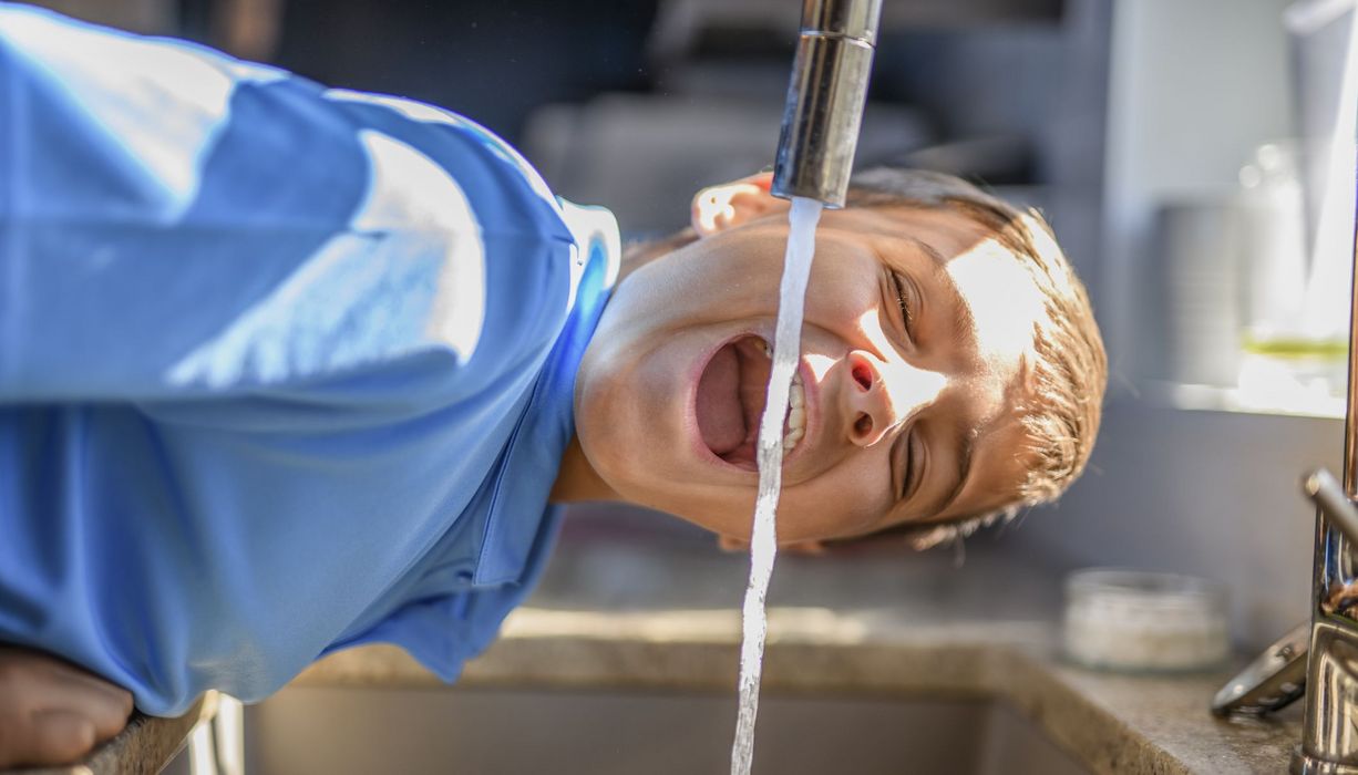 Junge, trinkt Wasser aus dem Hahn. 