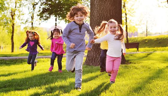 Fünf Kinder rennen über eine Wiese im Schatten eines Baumes.
