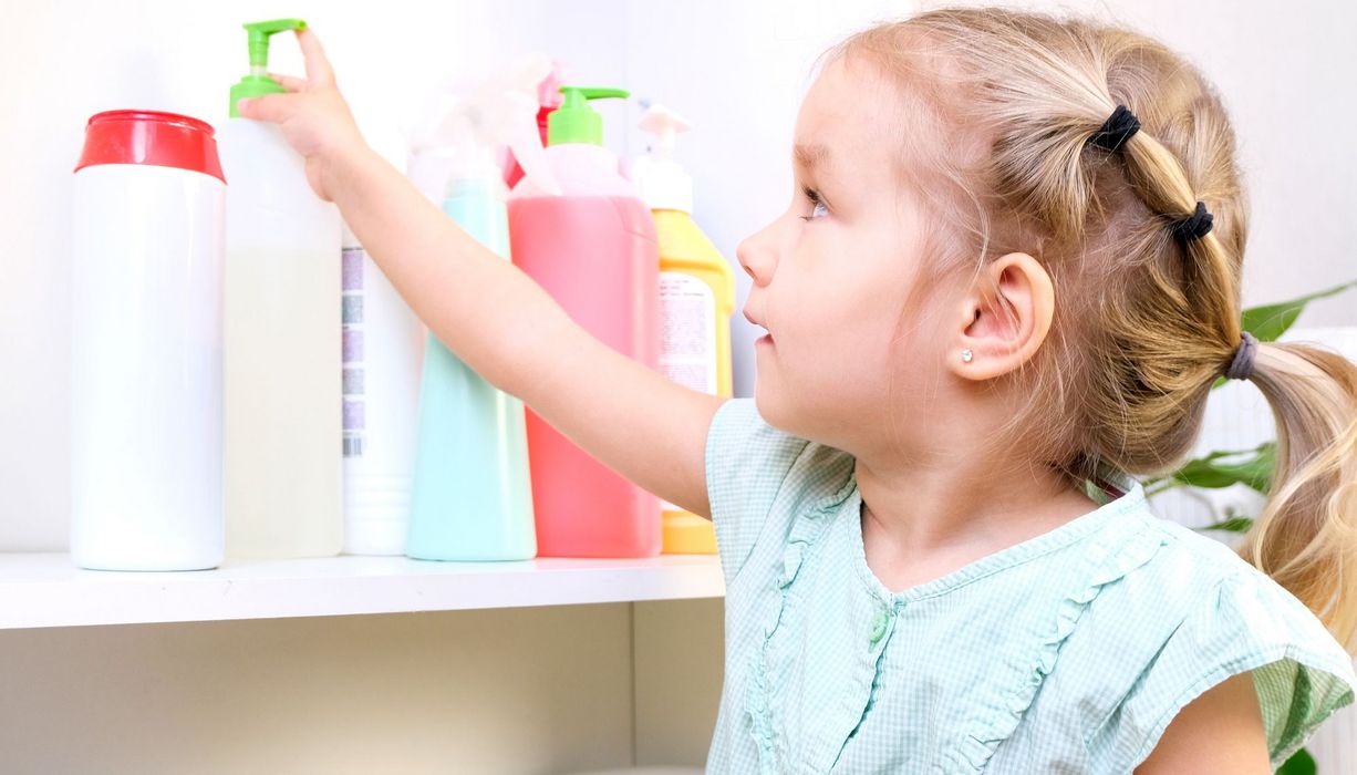 Ein Mädchen greift nach einer Flasche Putzmittel auf einem Regal.