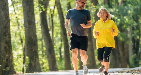Ein älterer Mann und eine ältere Frau joggen durch einen sommerlichen Wald