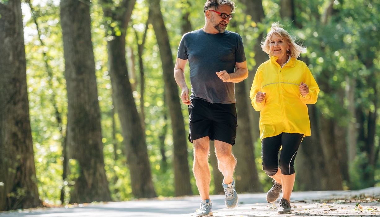 Ein älterer Mann und eine ältere Frau joggen durch einen sommerlichen Wald