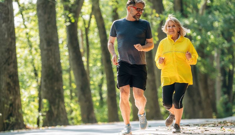 Ein älterer Mann und eine ältere Frau joggen durch einen sommerlichen Wald