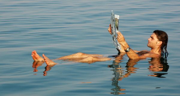 Mann liegt im Wasser und liest Zeitung.