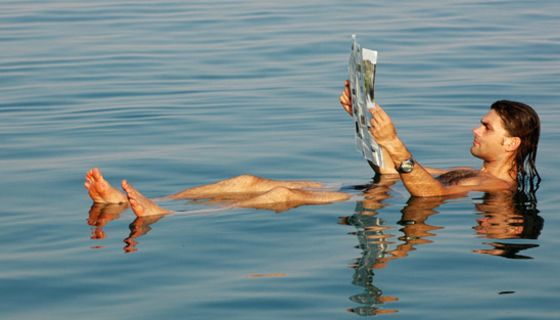 Mann liegt im Wasser und liest Zeitung.