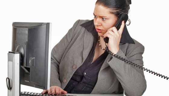 Übergewichtige Frau sitzt am PC und hat eine Telefon am Ohr