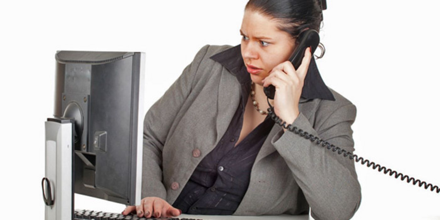 Übergewichtige Frau sitzt am PC und hat eine Telefon am Ohr