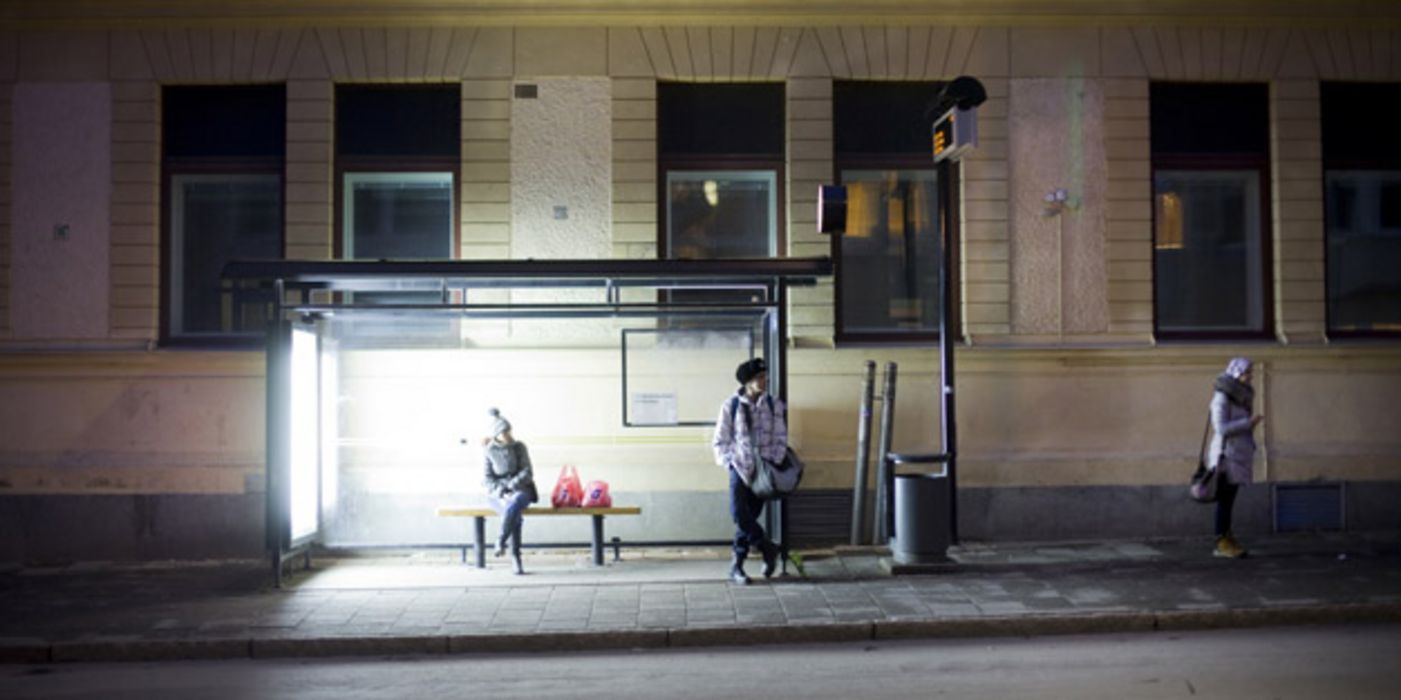 Menschen an hell beleuchteter Bushaltestelle in Umeå, Schweden.