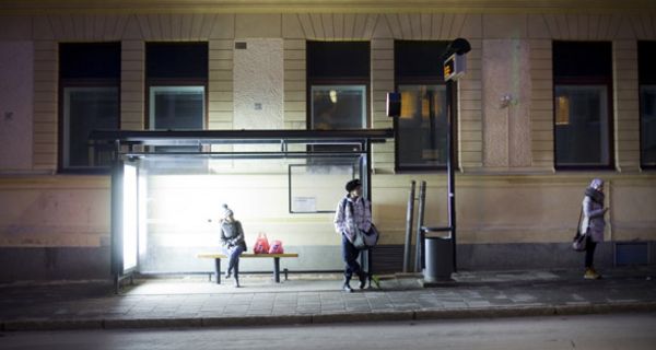 Menschen an hell beleuchteter Bushaltestelle in Umeå, Schweden.