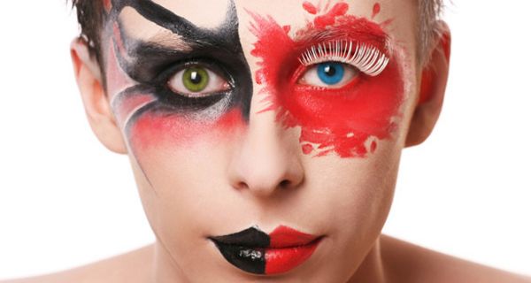 Frontalportrait Frau mit Kontaktlinsen eine grün, eine blau, schwarz-rot-flammiger Augenbemalung und schwarz-roten Lippen