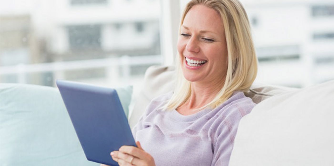 Lachende blonde Frau um die 40 mit Tablet-PC