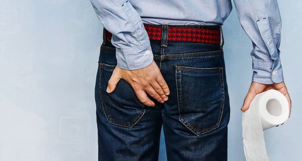 Rückenansicht eines Mannes mit einer Rolle Toilettenpapier in der Hand.