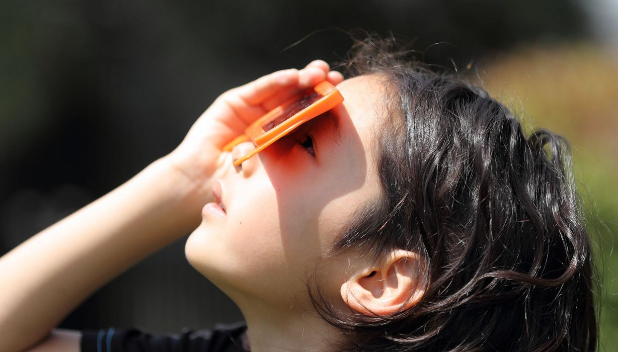 Kind, schaut durch eine spezielle Brille in die Sonne.