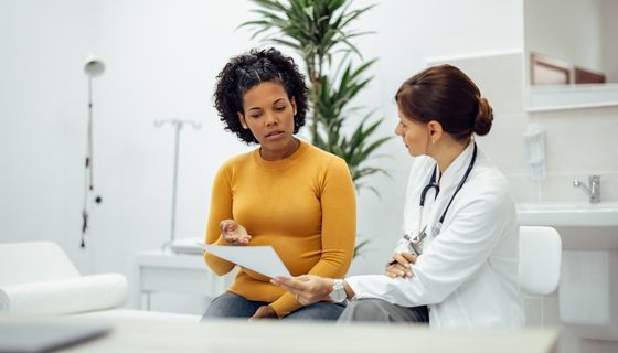 Eine Patienten und eine Ärztin sprechen miteinander und schauen auf ein Formular.