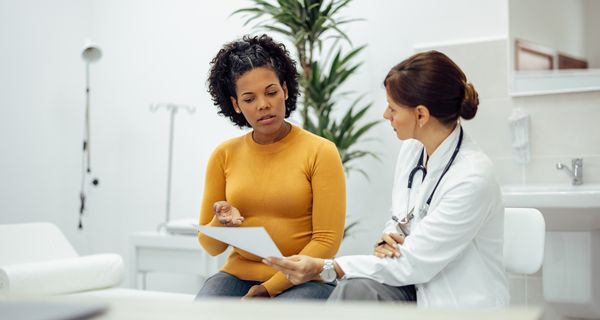 Eine Patienten und eine Ärztin sprechen miteinander und schauen auf ein Formular.