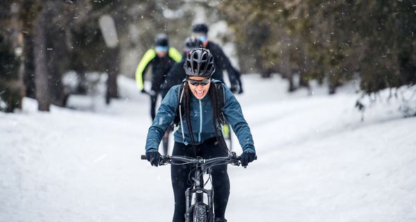 Frau fährt Fahrrad bei Schnee und lacht glücklich.