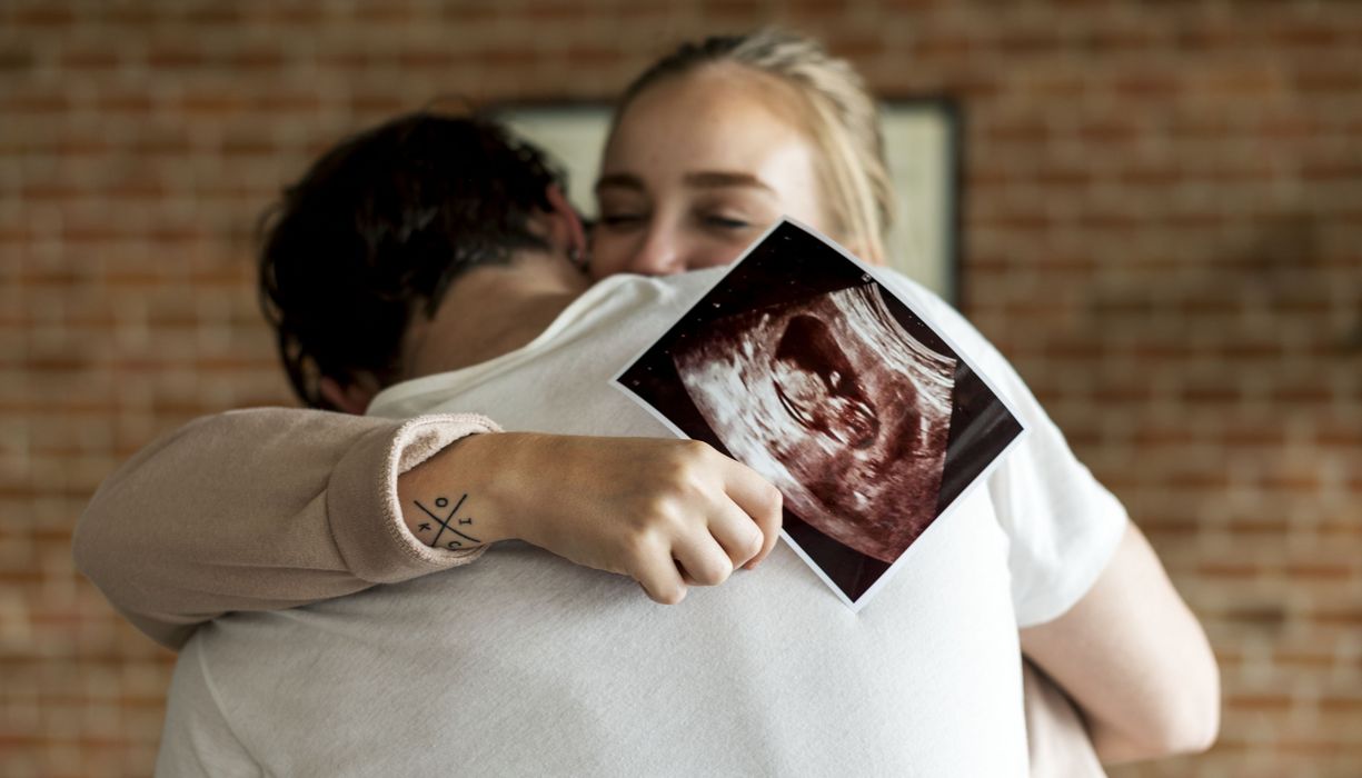 Paar, umarmt sich, Frau hält ein Ultraschall-Foto in der Hand.